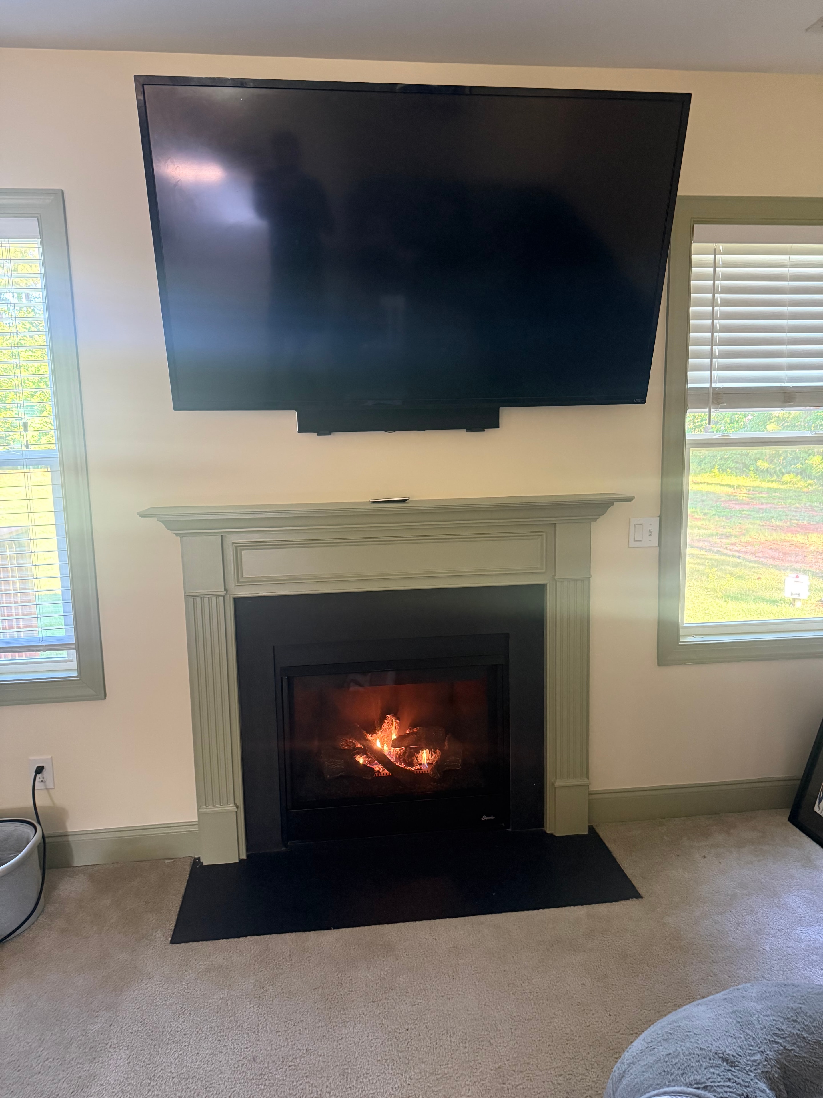 Gas fireplace with painted mantel burning in a living room alongside a wall-mounted TV